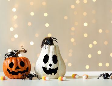 orange and white pumpkins with faces painted on them, sitting on a table with candy corn and spiders